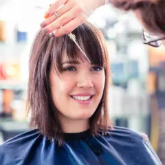 Une coiffeuse ajuste la frange d'une cliente souriante, finalisant une coupe carré.