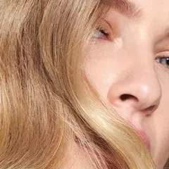 Un gros plan sur le visage d'une jeune femme aux yeux bleus et aux cheveux blond vénitien ondulés, encadrant son visage.