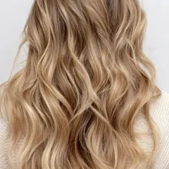 Chevelure ondulée aux reflets blonds subtils, un effet babylight blond naturel et lumineux.