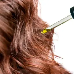 Une goutte d'huile tombe sur des cheveux bruns. Un geste simple pour mettre de l'huile sur les cheveux tous les jours pour les nourrir.