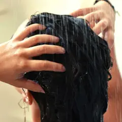 Mains massant des cheveux mouillés sous la douche, comme un soin au beurre de karité cheveux sans rinçage pour une douceur intense.