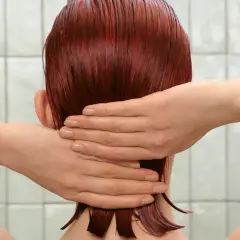 Mains massant des cheveux roux mouillés, peut-être après l'application d'un shampoing violet pour raviver la couleur.