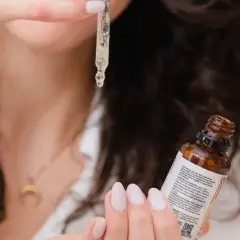 Une femme montre comment appliquer un sérum avec une pipette, une goutte dorée tombant sur sa main.