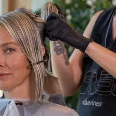 Une coiffeuse applique une couleur ou une mèche pour cacher les cheveux blancs d'une cliente.