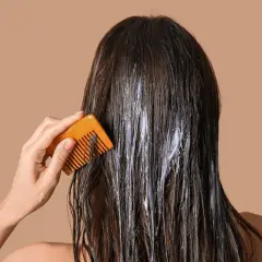 Application d'une coloration végétale sur cheveux. Une main peigne doucement les mèches pour répartir le produit.
