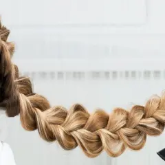 Une main peigne une tresse blonde, une coiffure originale facile à réaliser pour un look sophistiqué.