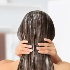 Application d'un soin pour une clarification cheveux. Les mains appliquent le produit sur les longueurs.