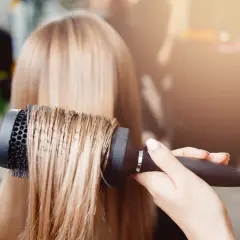 Main d'un coiffeur effectuant un brushing sur des cheveux blonds.