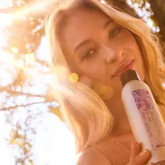 Une femme aux cheveux blonds, avec un balayage naturel, tient un produit Davines sous un soleil éclatant.