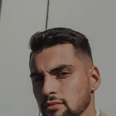 Un homme au chignon homme rasé, regard intense, sous un soleil éclatant.