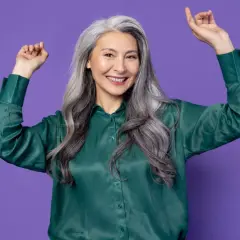 Une femme de 65 ans rayonnante avec une chevelure argentée, portant une chemise verte, célèbre la beauté naturelle.