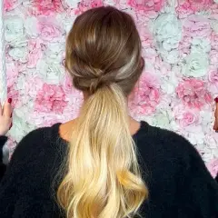 Coiffure semi attachée élégante avec une tresse torsadée, sur fond de mur de fleurs roses et blanches.