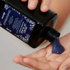 Une main verse un shampoing bleu, idéal pour les cheveux blonds, dans une autre main.