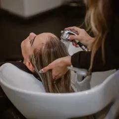 Une femme se fait laver les cheveux dans un salon de coiffure. La question est : combien de fois se laver les cheveux par semaine ?
