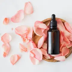 Flacon d'huile essentielle sur un lit de pétales de rose, idéal pour les cheveux gras.