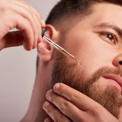 Un homme applique de l'huile de ricin sur sa barbe avec un compte-gouttes pour une pousse plus dense et soyeuse.