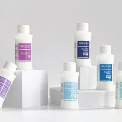 Six bouteilles de produits capillaires Kerasoin, dont un révélateur couleur, disposées sur des cubes blancs.