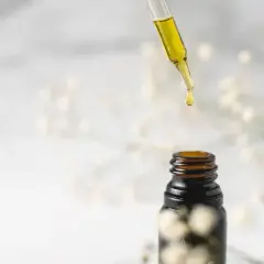 Goutte d'huile de jojoba tombant d'une pipette sur un flacon ambré. Idéal pour des cheveux transformés, avant après.