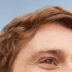 Un homme au regard clair, ses cheveux châtains légèrement ondulés, un brushing naturel.