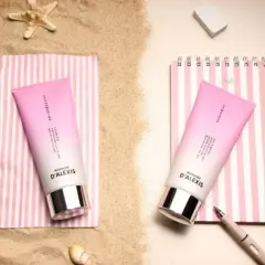 Deux tubes de crème rose sur des serviettes rayées, parfaits pour hydrater les cheveux sec après une journée à la plage.