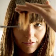 Une femme se coupe les pointes des cheveux. Elle hésite sur combien de cm couper.