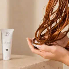 Mains douces appliquant un soin sur des cheveux bouclés roux, avec des produits Tokio Inkarami. Idéal pour la décoloration cheveux bouclés.