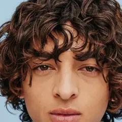 Gros plan sur un visage aux yeux marron et à la coiffure cheveux frisés bruns et volumineux.