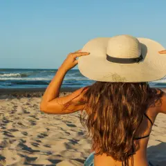 Une femme à la plage, coiffée d'un grand chapeau, montre comment protéger ses cheveux du soleil.