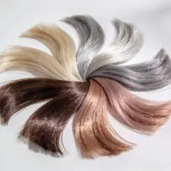 Échantillons de cheveux aux teintes variées, du brun au blond platine, disposés en éventail. Un fond d'éclaircissement subtil met en valeur les reflets chatoyants.
