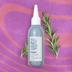 Flacon d'huile de romarin pour la pousse des cheveux, entouré de brins de romarin frais sur fond pailleté rose et violet.