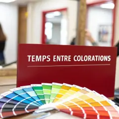 Un éventail de couleurs de cheveux et un panneau "Temps entre colorations sans ammoniaque" dans un salon de coiffure.