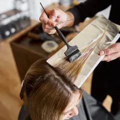 Coiffeur appliquant de la poudre décolorante et oxydant 30 dosage sur des mèches de cheveux, préparant une transformation capillaire.