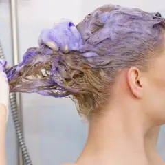 Une femme se lave les cheveux avec du shampoing bleu. Elle porte des gants pour savoir comment enlever le shampoing bleu sur les cheveux.
