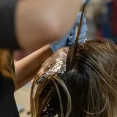 Application d'une patine Dialight sur des mèches de cheveux. Une main gantée applique le produit à l'aide d'un pinceau.