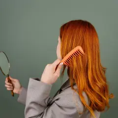 Femme rousse se coiffant, regardant dans un miroir. Elle cherche une solution pour enlever les reflets roux avec du citron.