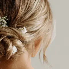 Chignon flou et romantique sur cheveux mi-longs, orné de petites fleurs blanches.
