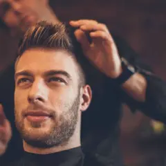 Un homme au regard pensif se fait coiffer une coupe pompadour par un barbier.