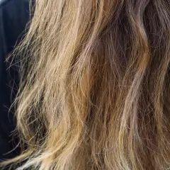Cheveux longs et ondulés, d'une teinte châtain clair avec des reflets blonds, prêts à teindre ses cheveux en blanc pour un look audacieux.