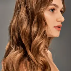 Une femme aux cheveux châtains ondulés, une transformation réussie de blonde à brune, pose de profil.