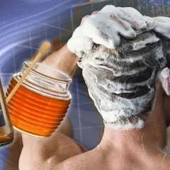 Une personne se lave les cheveux moussants, avec une bouteille de vinaigre de cidre et un pot de miel à proximité, pour éclaircir ses cheveux naturellement.