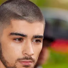 Un jeune homme au regard intense arbore une coupe buzz, ses cheveux courts et nets accentuent son style moderne.