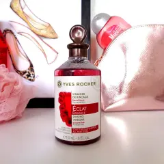 Bouteille de vinaigre de framboise pour cheveux Yves Rocher, avec des chaussures stylisées et une trousse de toilette rose en arrière-plan.