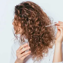 Une femme applique une huile sur ses cheveux bouclés frisottis pour les hydrater.