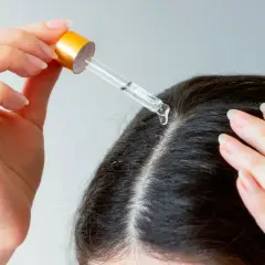 Une main applique une goutte d'huile de chanvre sur le cuir chevelu, une solution naturelle pour les cheveux blancs.