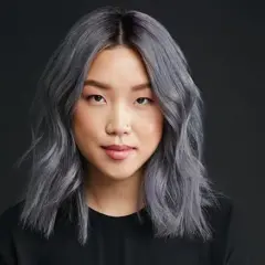 Une jeune femme au teint clair arbore une chevelure mi-longue, ondulée et d'un magnifique gris argenté. Elle porte un haut noir.