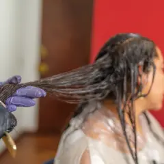 Application d'une patine sur cheveux humides. Une main gantée sépare une mèche pour une application uniforme.