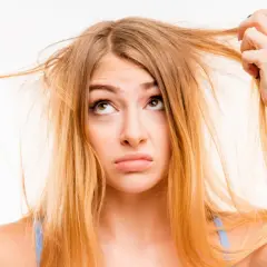 Une jeune femme aux cheveux jaune regarde ses mèches emmêlées avec une expression perplexe.