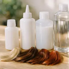 Échantillons de cheveux blonds, bruns et roux devant des bouteilles, prêts pour une coloration avec un oxydant.