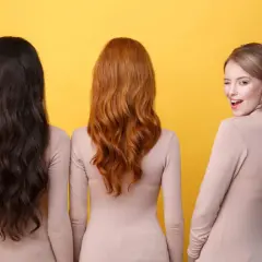 Trois femmes se tiennent côte à côte, montrant la diversité de la couleur cheveux femme : brun foncé, roux flamboyant et blond rosé.