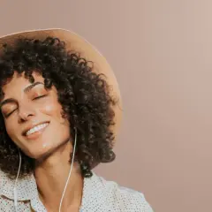 Femme avec une permanente naturelle, un chapeau et des écouteurs, profitant d'un moment de détente.